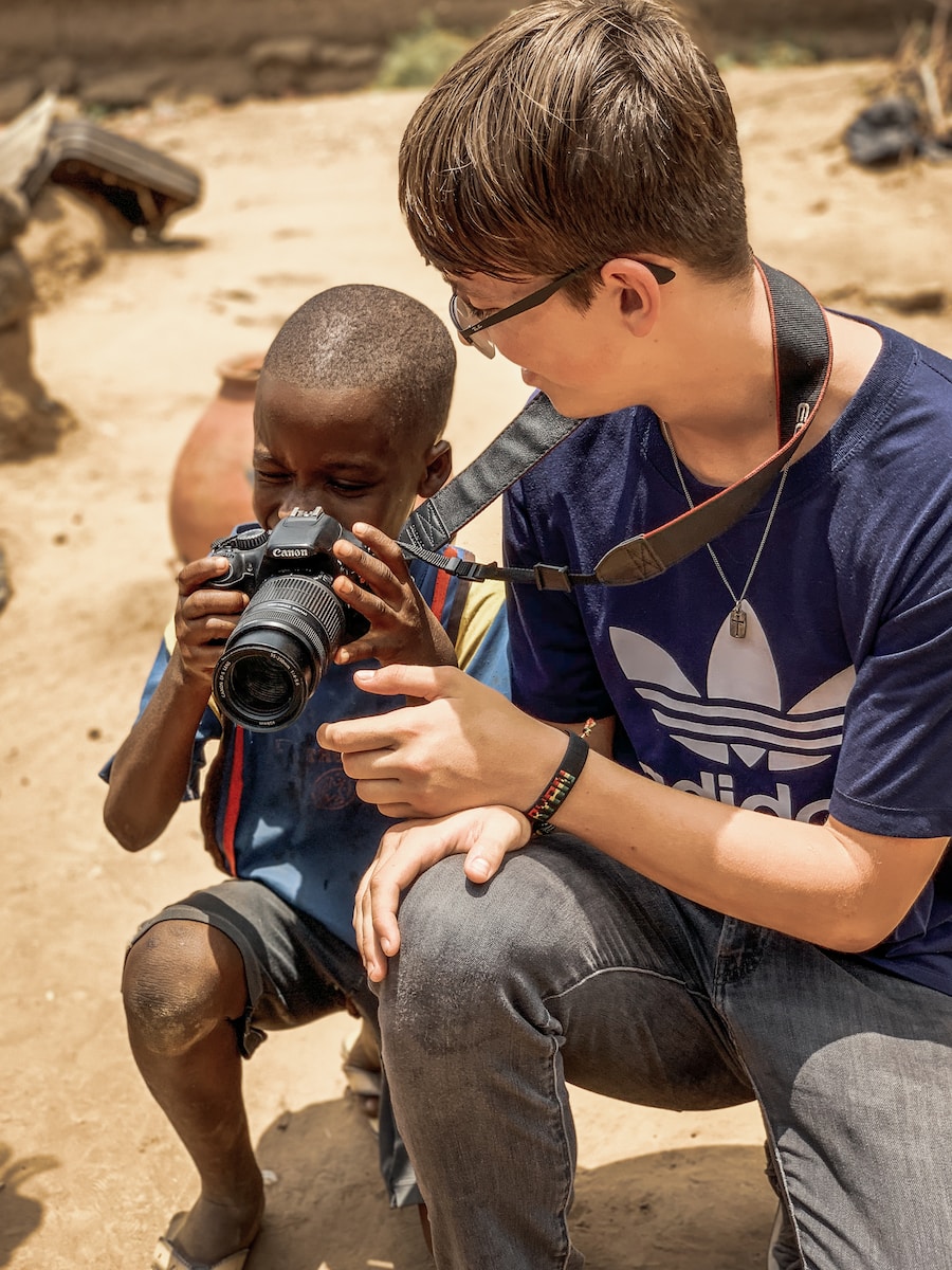 boy taking a knee and holding DSLR camera beside man taking a knee
