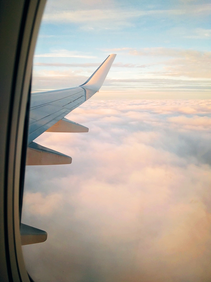 Wing of aircraft flying over clouds at sundown