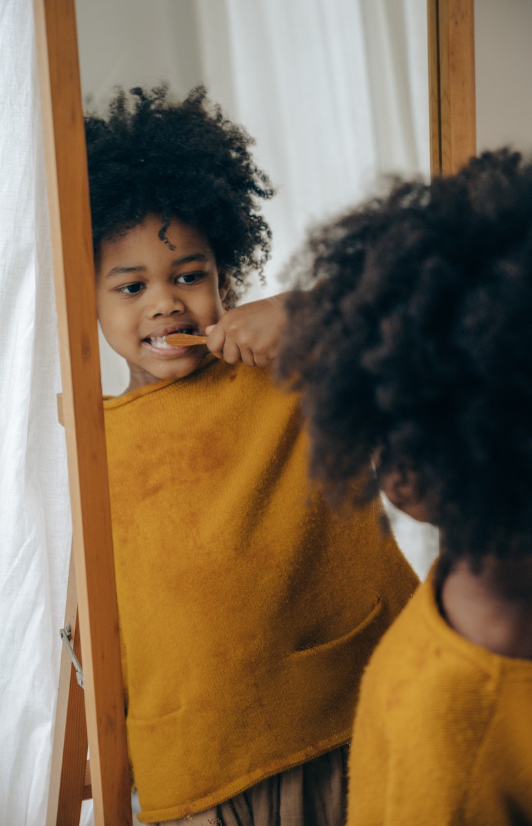 Cheerful boy brushing teeth against mirror