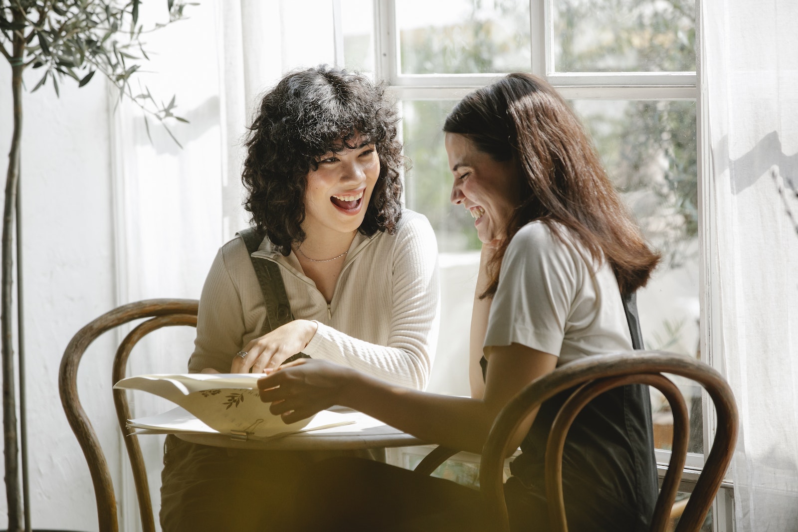 Laughing multiracial female colleagues wearing uniform flipping pages of papers while discussing work together