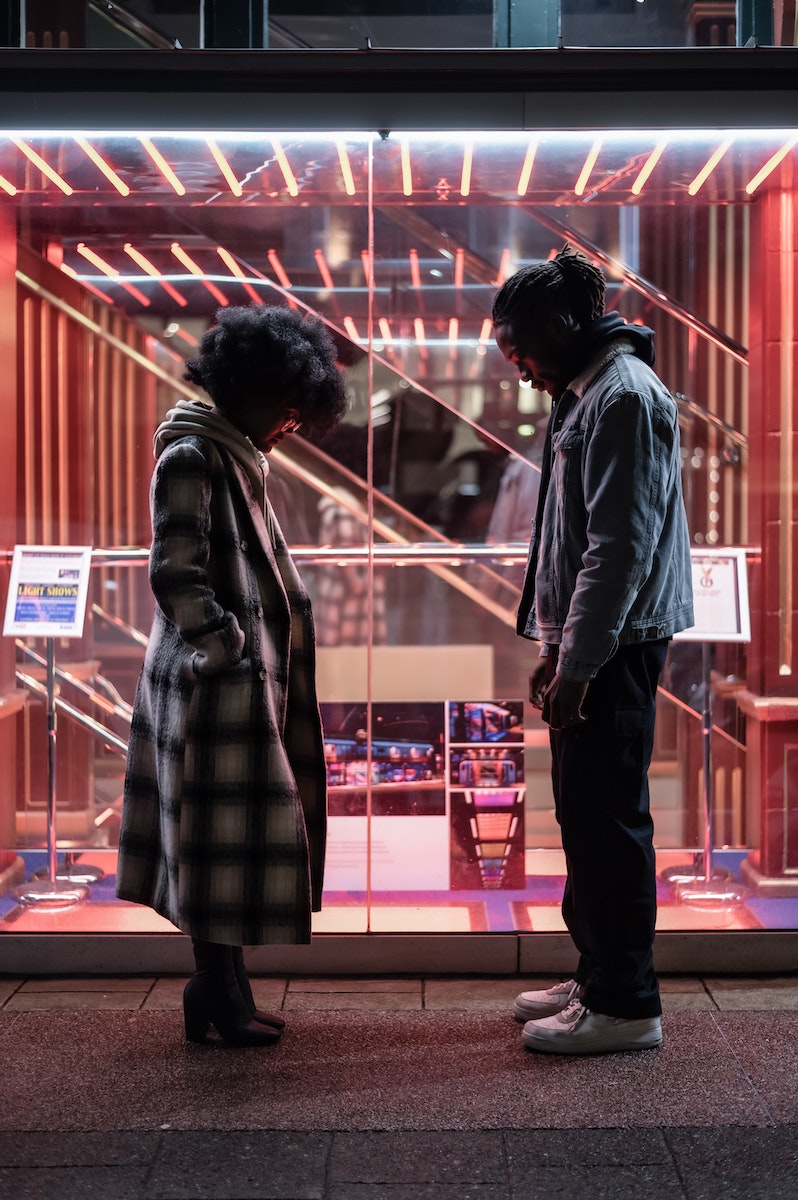 Side view full body of misunderstanding African American couple standing opposite to each other and looking down at night