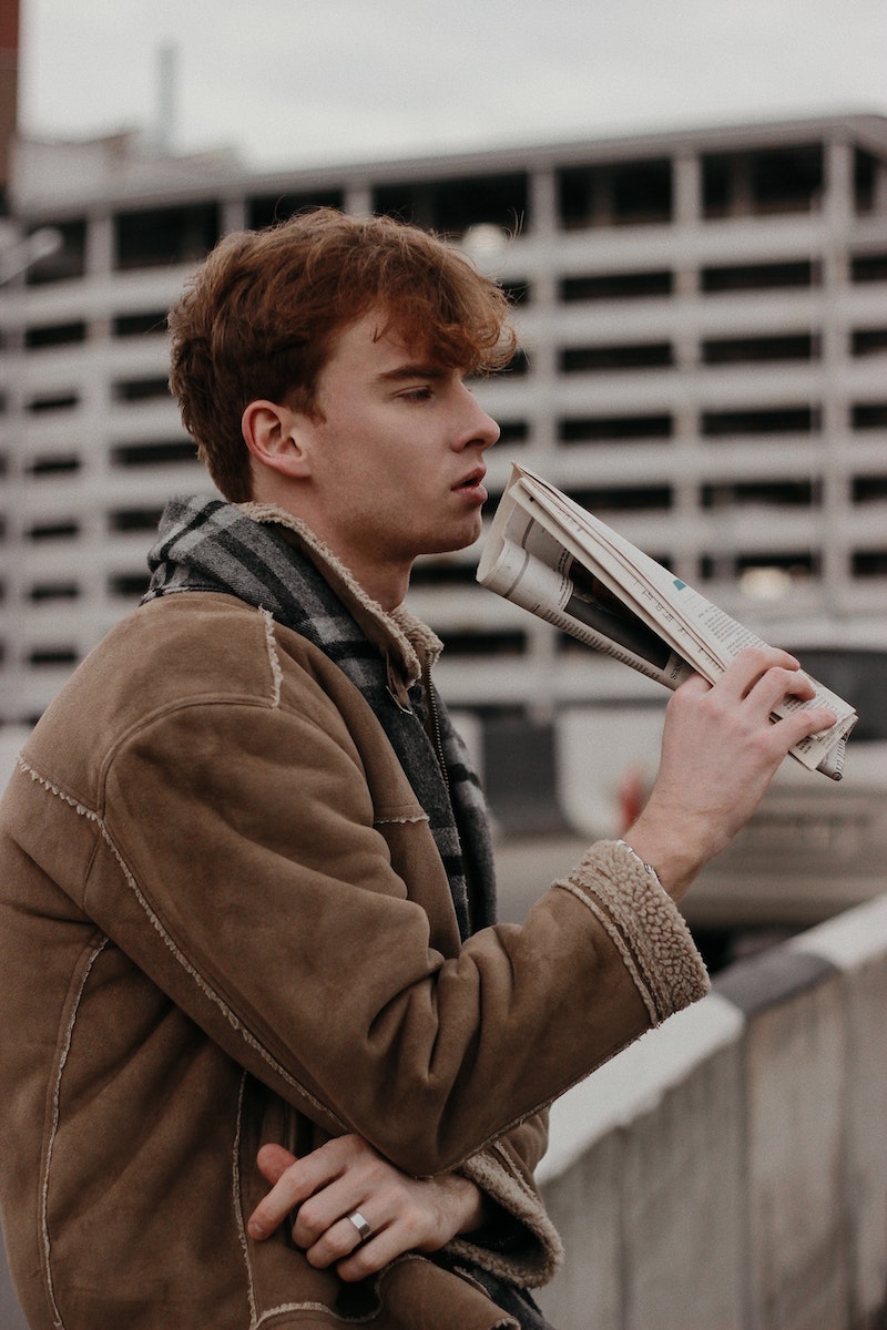 Man in Brown Jacket and Gray Muffler Holding a Newspaper