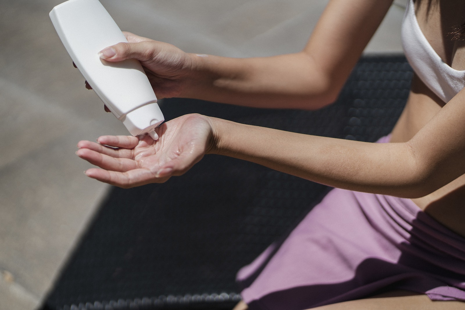 Faceless woman applying lotion on hand on sunny day