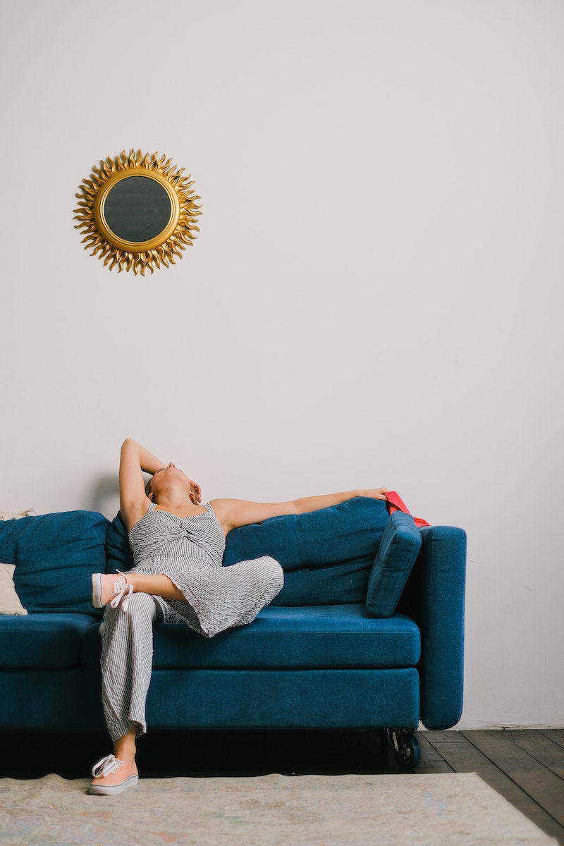 Unrecognizable exhausted woman with rag touching head while leaning back on couch after housework in living room