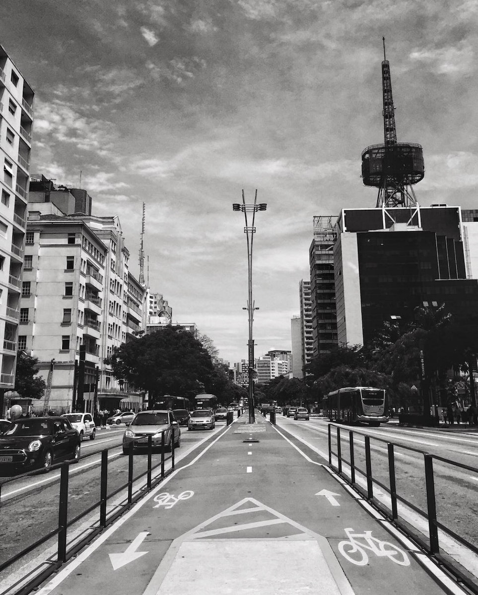 Black and white cityscape with asphalt road going along buildings and cycle lane in middle
