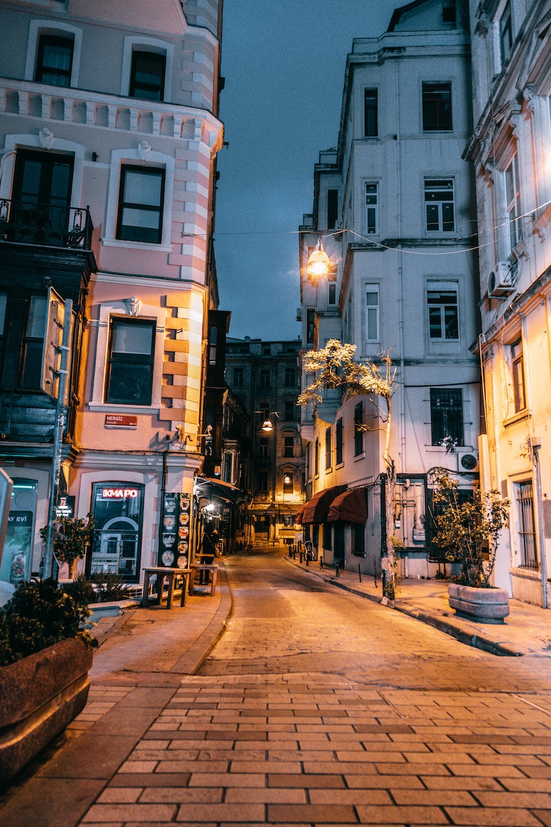 Empty cobblestone city street between aged residential houses with glowing lamps at night