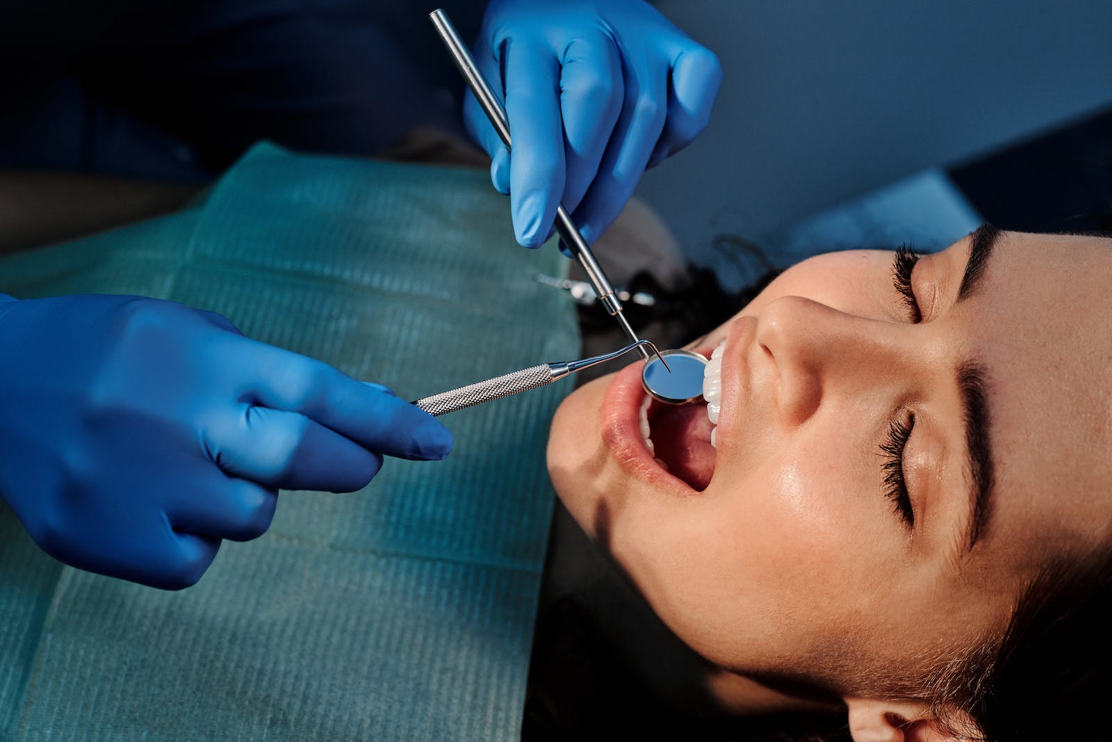 A Person Wearing Blue Latex Gloves Holding a Mirror in a Woman's Mouth