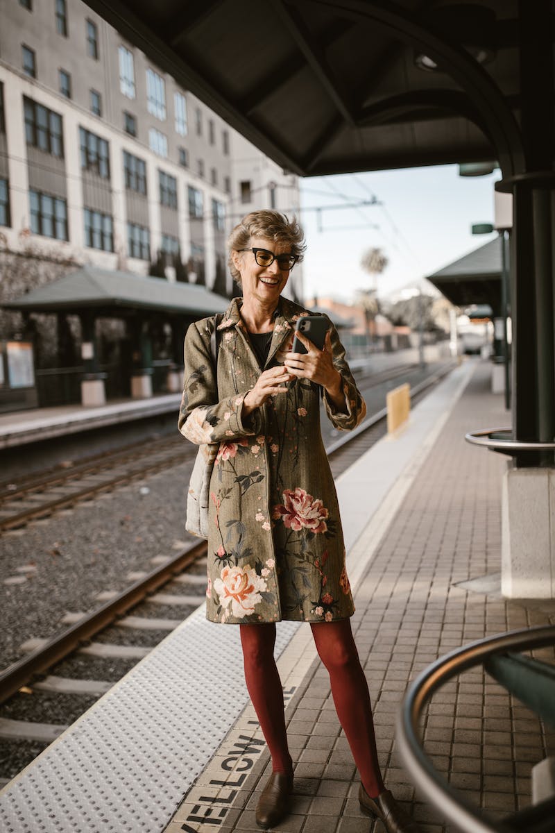 Woman in Floral Dress Standing on Railway Platform Using Cellphone
