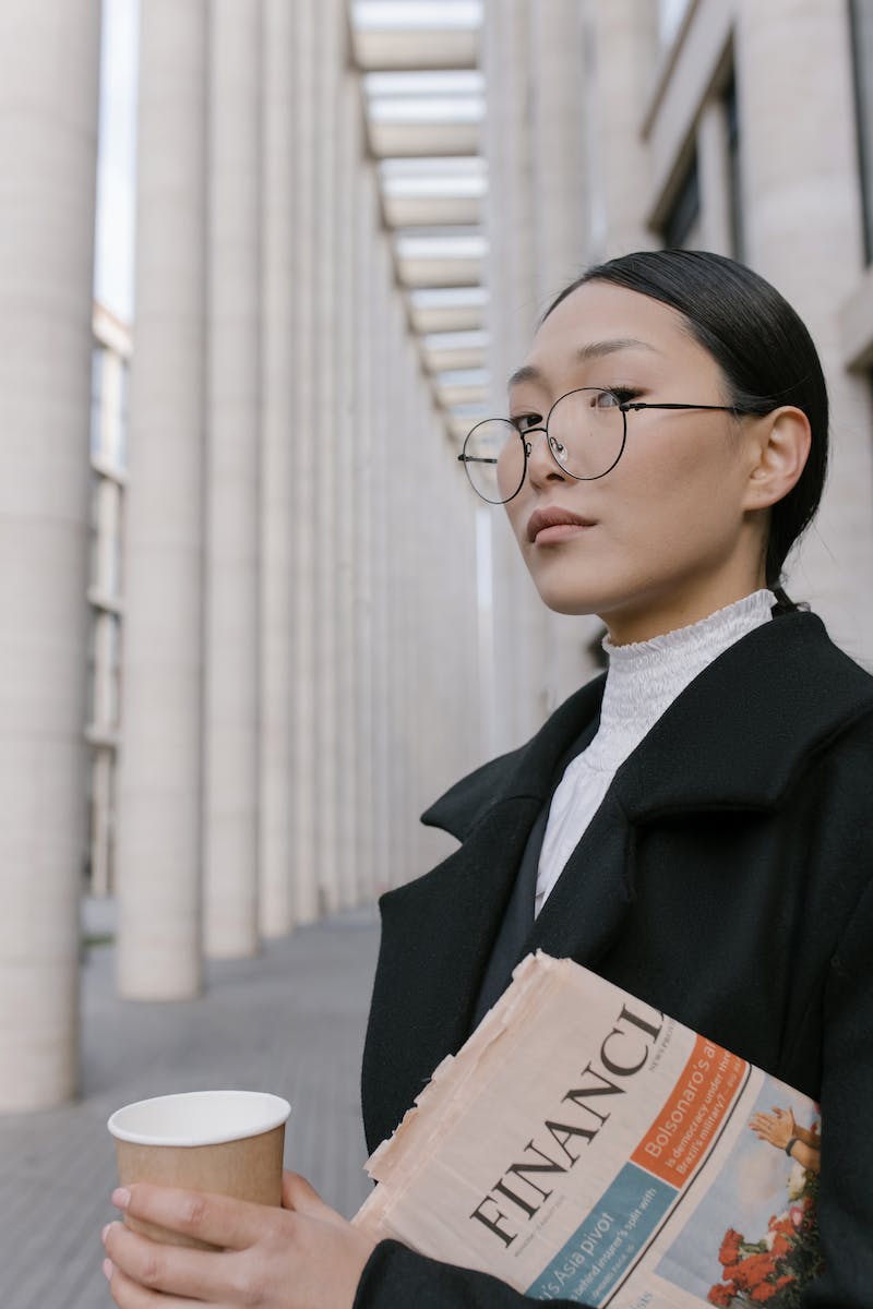 A Woman in Black Coat Wearing Eyeglasses while Holding a Cup of Coffee