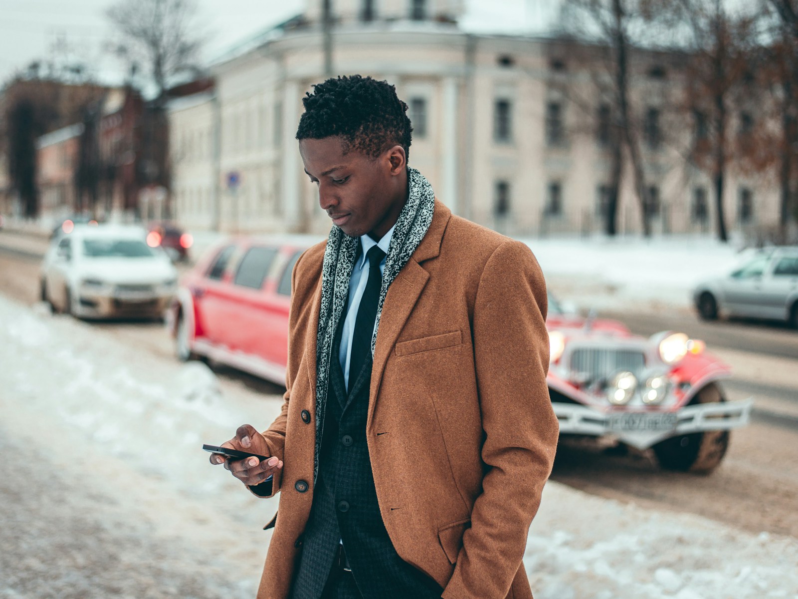 man wearing brown two-button dress jacket holding Android phone