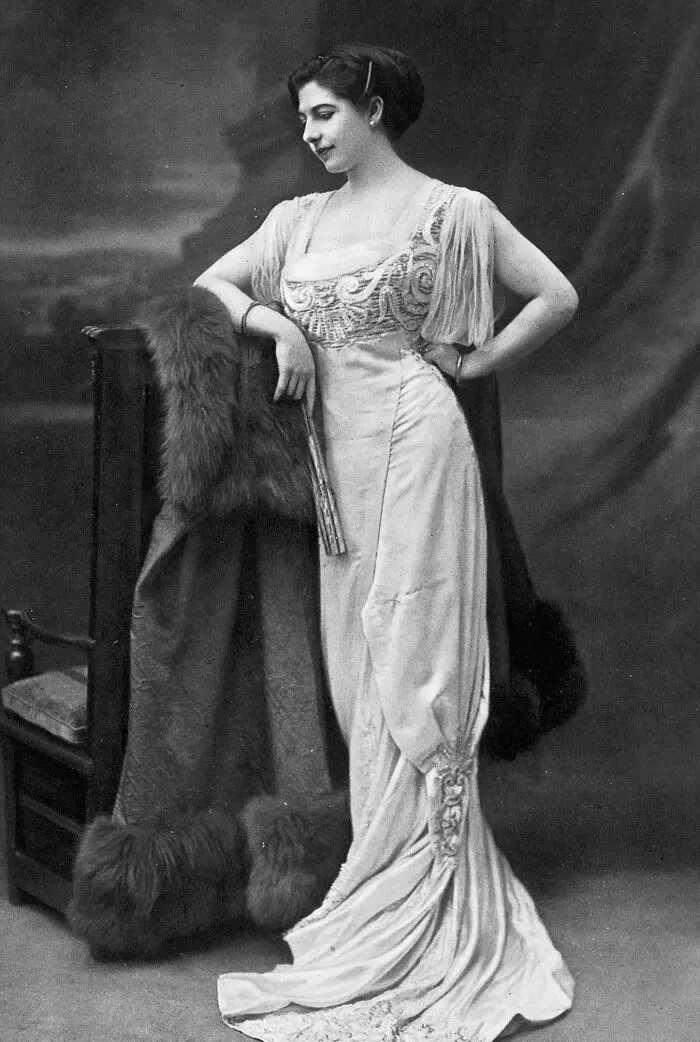 Elegantná dáma v historickej róbe pri operadle, čiernobiela fotografia, dobový štýl.