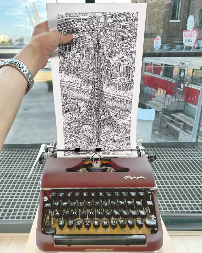 Písací stroj s kresbou Eiffelovej veže na vloženom papieri, rukou držiacou papier.