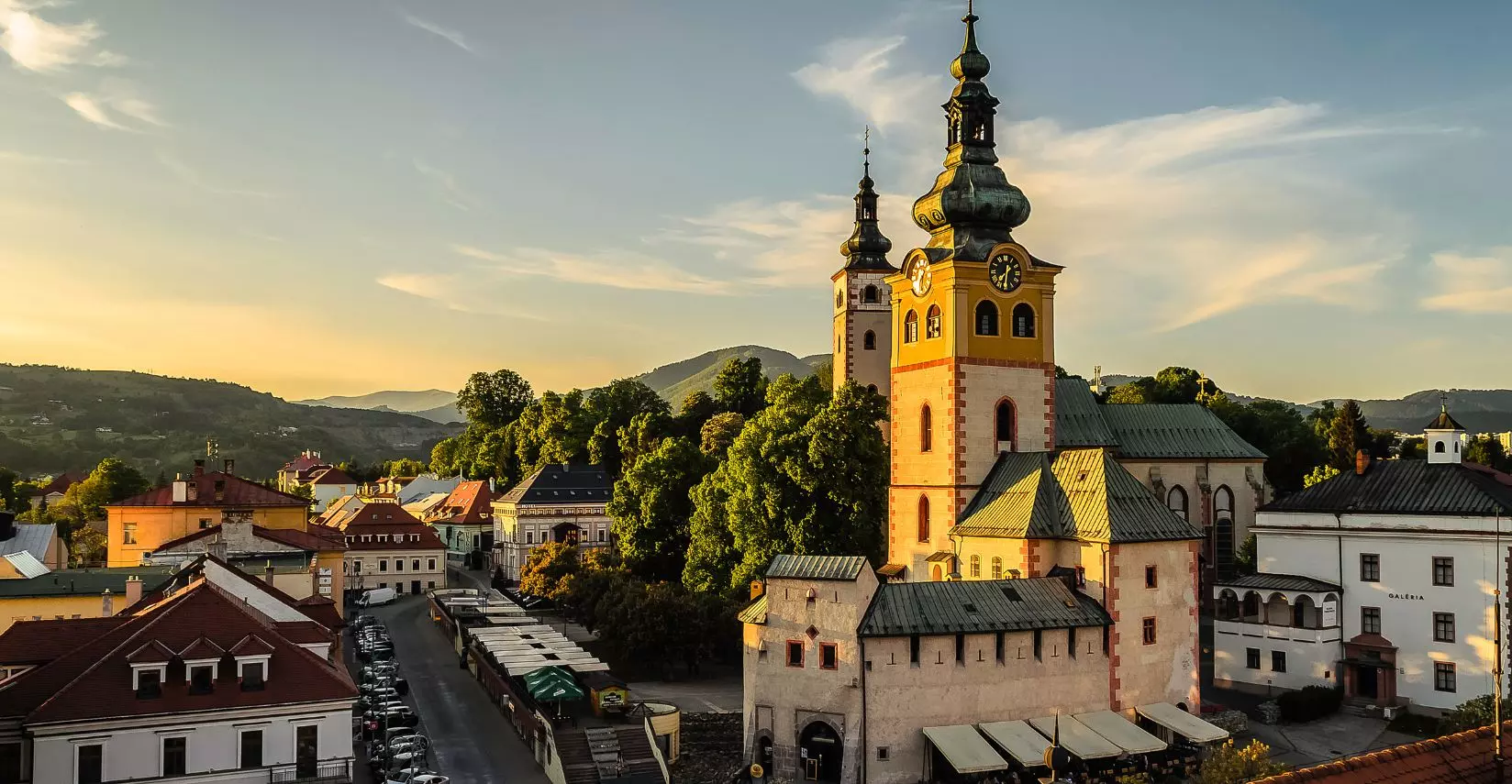 Historické centrum s vežou a horami v pozadí pri západe slnka, pokojná atmosféra Banskej Bystrice v prírode.