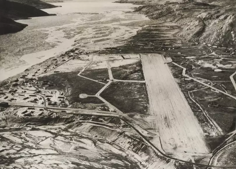 Letecká snímka historického letiska v horskej oblasti pri vodnej ploche, zachytáva rané štádium infraštruktúry.
