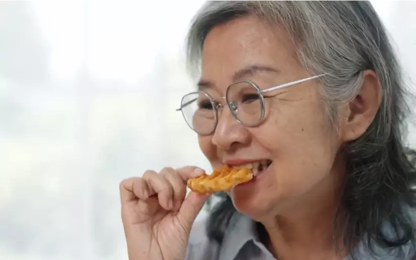 Žena s okuliarmi si vychutnáva kúsok pizze v jasnom prostredí.