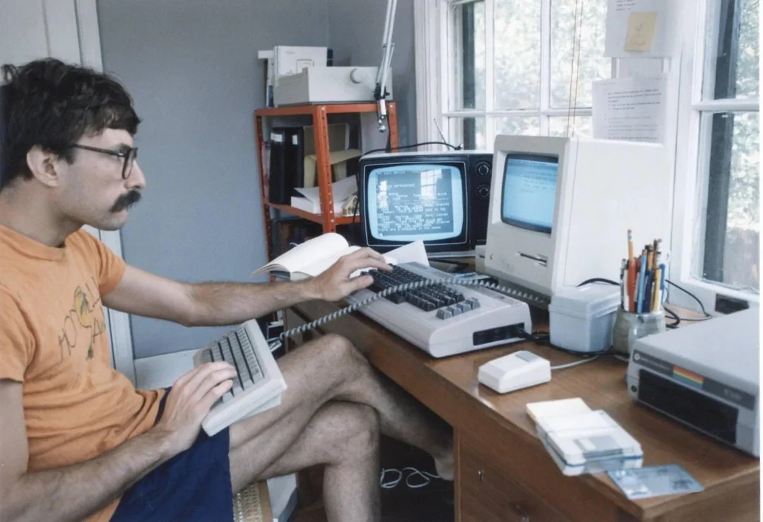 Muž pracujúci na starom počítači s viacerými obrazovkami v retro kancelárii pri okne.
