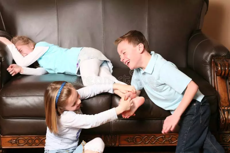 Deti sa smejú a hrajú na pohovke, jedno dieťa leží, ďalšie dve ju šteklením rozveseľujú.