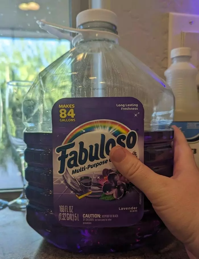 Veľká nádoba s čistiacim prostriedkom Fabuloso s levanduľovou vôňou, držiaca ruka, kuchynská linka na pozadí.
