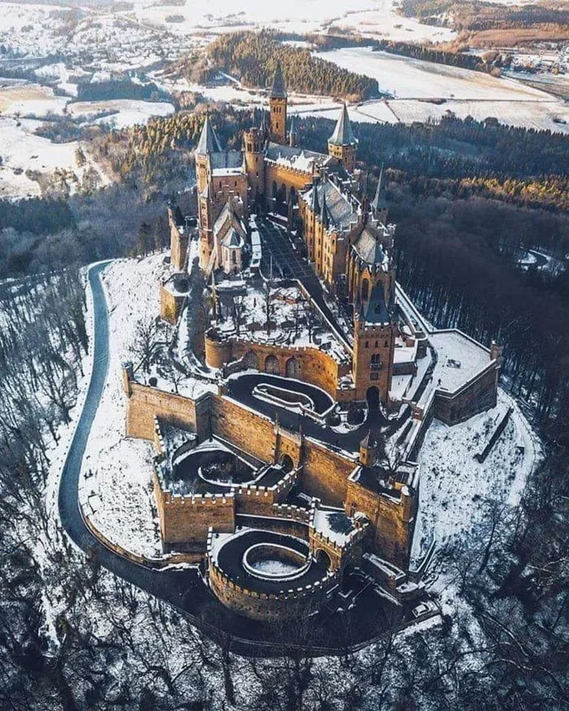 Letecký pohľad na zasnežený stredoveký hrad obklopený lesmi v zime.