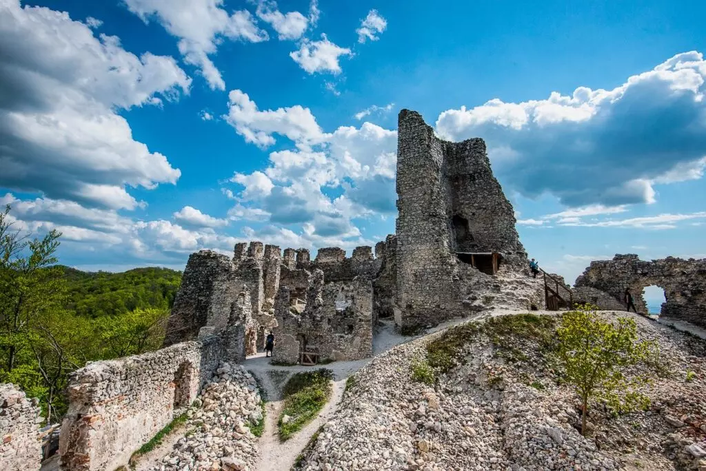 Hradné ruiny v zelenom prostredí pod modrou oblohou s bielymi oblakmi.
