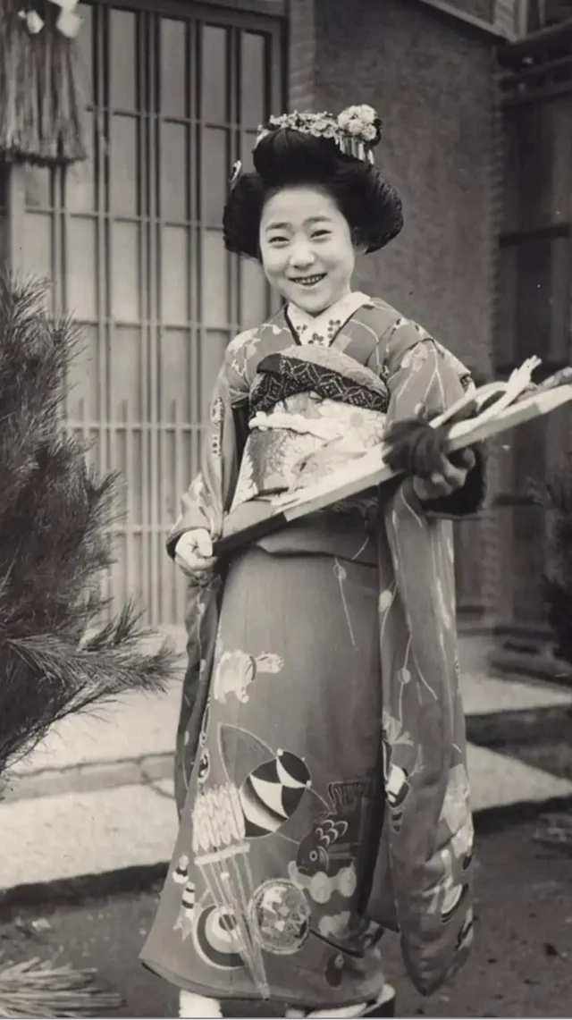 Japonská žena v tradičnom kimone s úsmevom stojí vonku pri rastline.