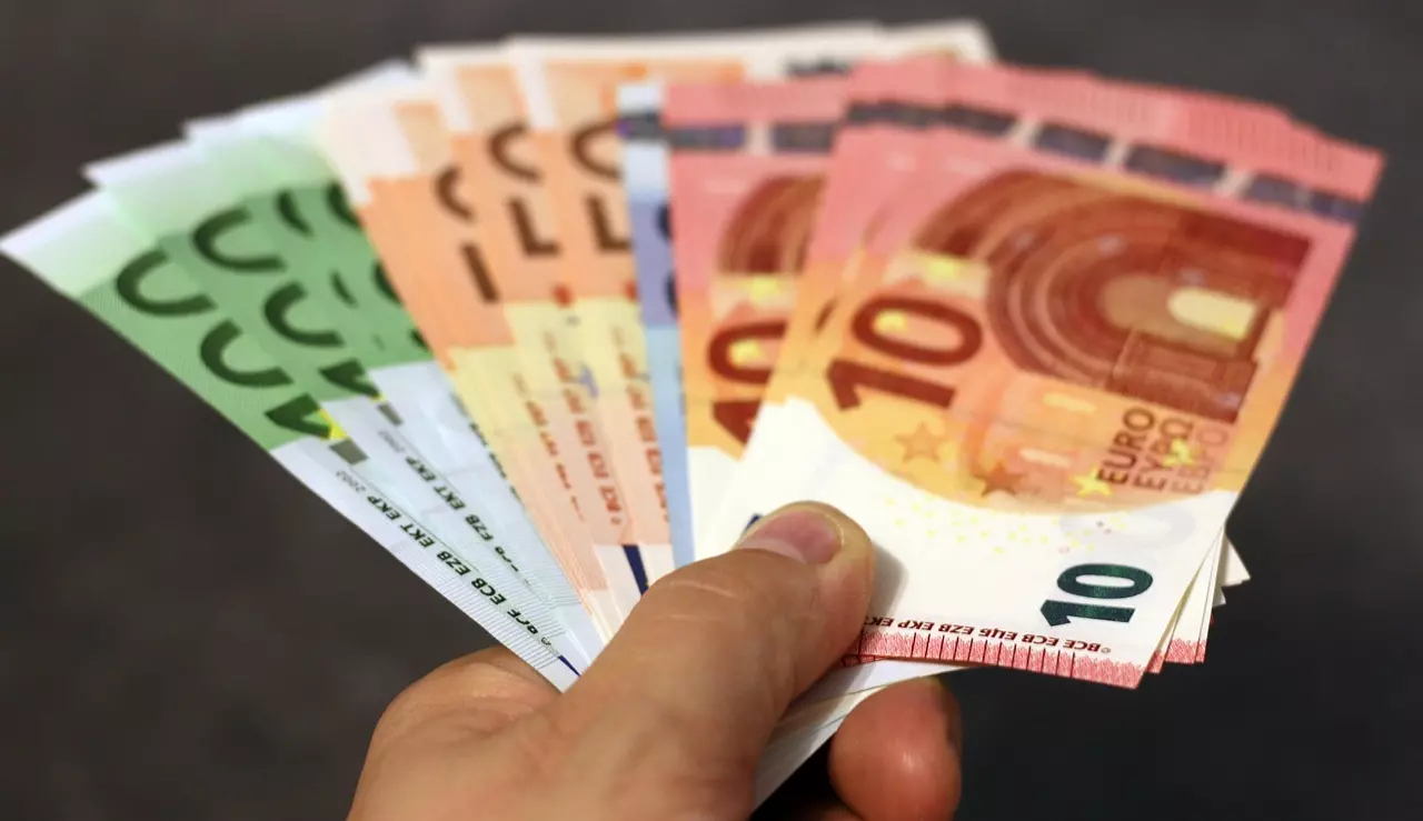 Osoba drží vejárovito rozložené eurobankovky rôznych hodnôt na šedom pozadí.