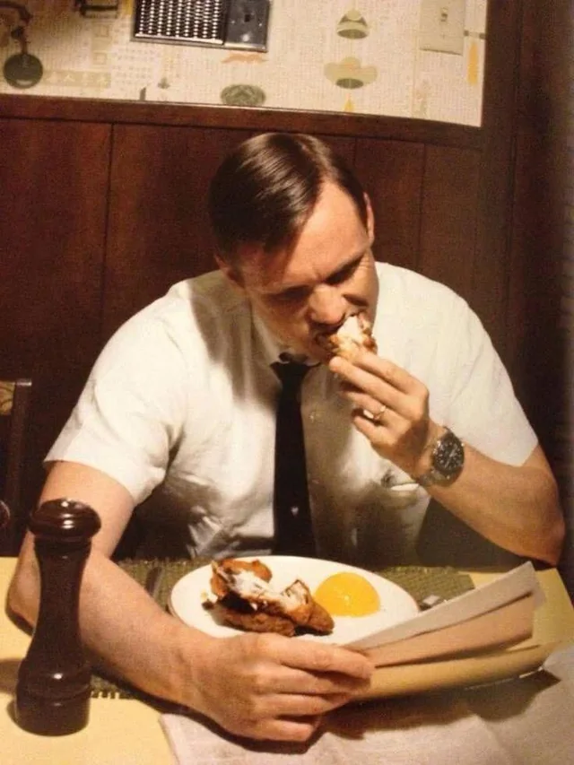 Muž pri stole raňajkuje smažené kurča a číta noviny v retro kuchyni.