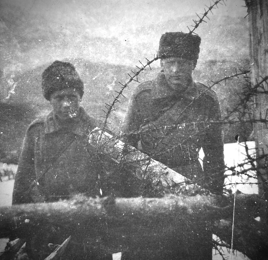 Dva osoby v zimnom oblečení pri zamrznutej barikáde počas zasneženého dňa, čiernobiela historická fotografia.
