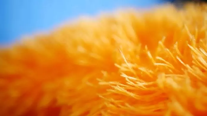 Oranžové vlákna textílie v detailnom zábere, pôsobí mäkko a príjemne v kombinácii s modrým pozadím.