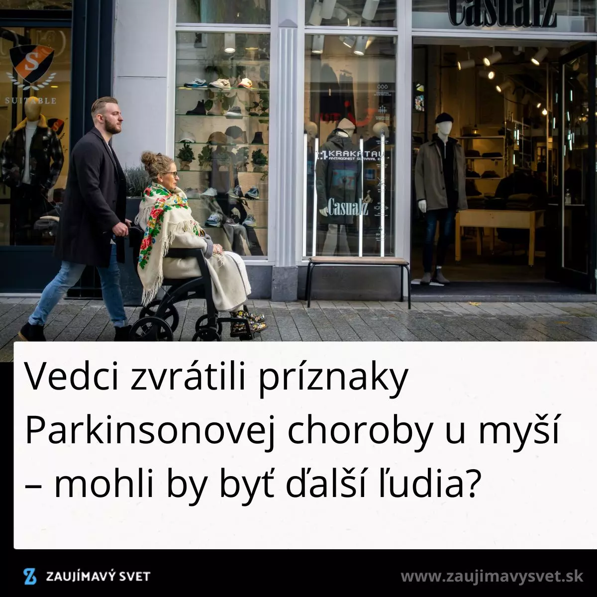 Muž tlačí ženu na invalidnom vozíku po ulici pred obchodom s oblečením.