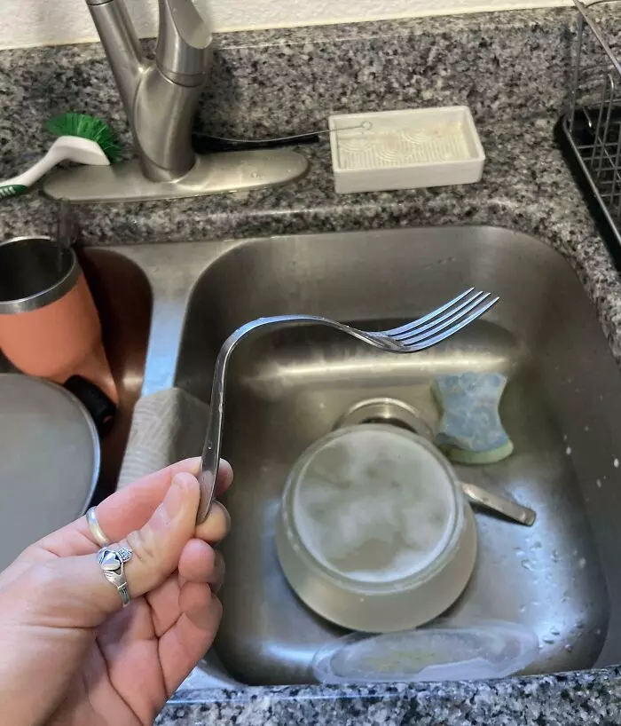 Pohľad na vidličku ohnutú neobvykle v umývadle plnom riadu.