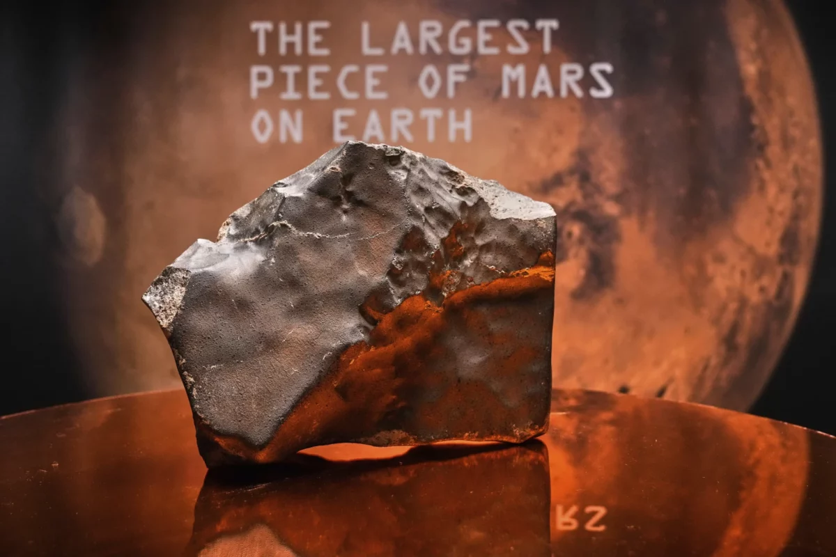 Kus marťanského meteoritu v múzeu na pozadí planéty Mars, vystavený ako najväčší kus na Zemi.