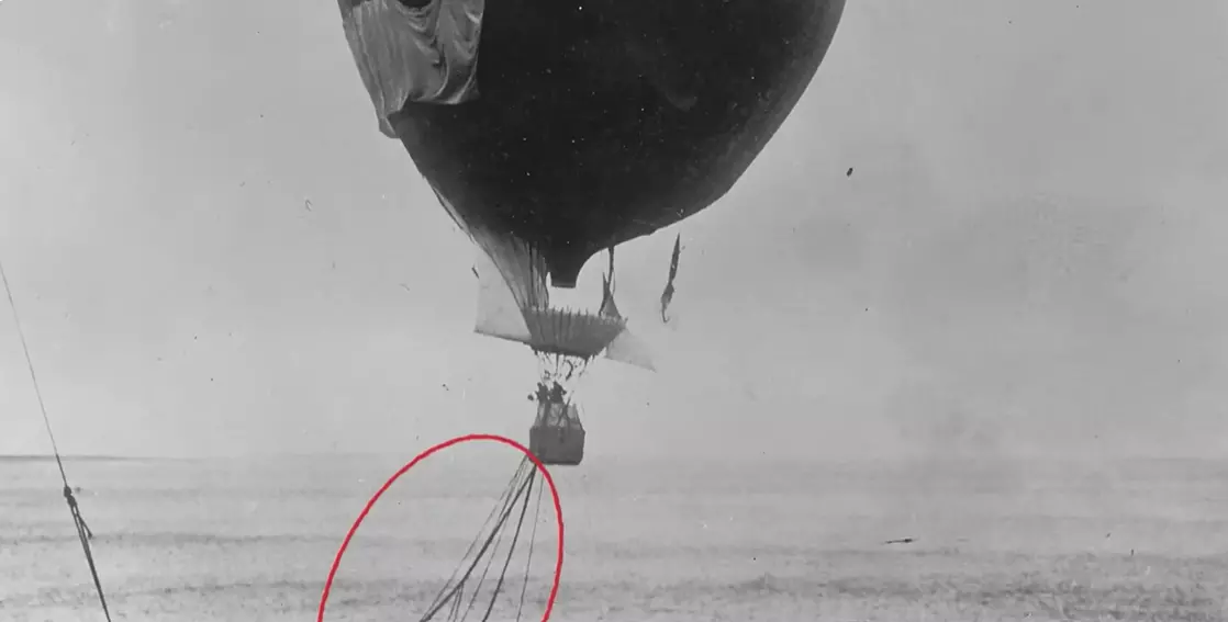 Historická čiernobiela fotografia balóna nad morom s pripojenými lanami.