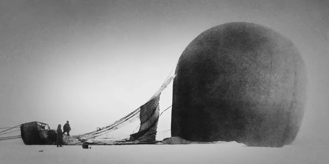 Histórická fotografia nafukovania teplovzdušného balóna na zasneženej krajine so sledom dvoch mužov pri koši.