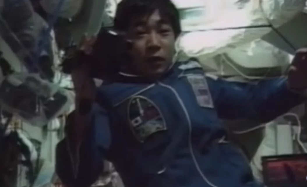 Astronaut v modrej uniforme pracuje na vesmírnej stanici, plávajúci v prostredí bez gravitácie.