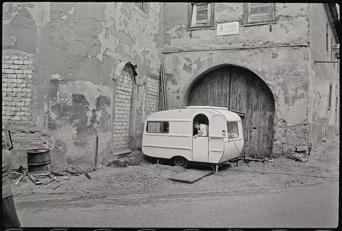 Starý karavan zaparkovaný pri historickej budove s opotrebovanou omietkou a veľkou drevenou bránou.
