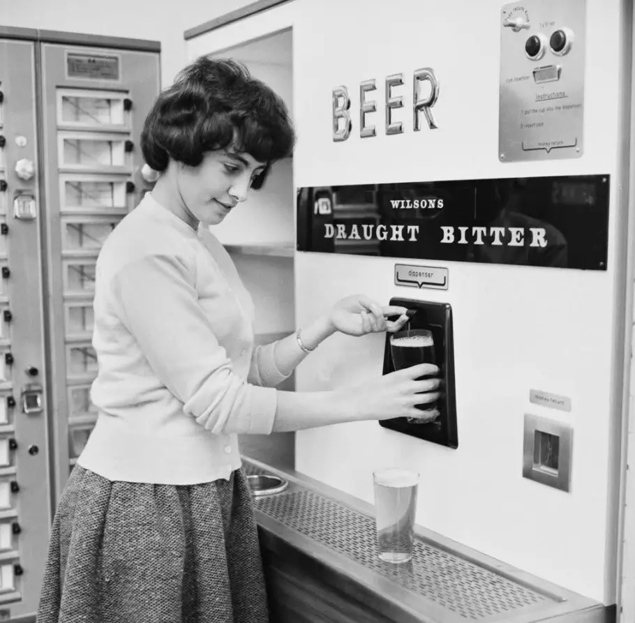 Žena čapuje pivo z retro automatu na nápoje, nad ktorým je nápis Beer.