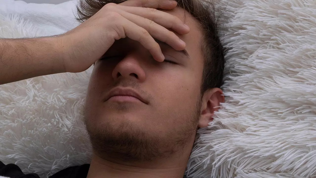 Osoba leží na pohovke a drží si hlavu, vyjadruje únavu alebo stres.