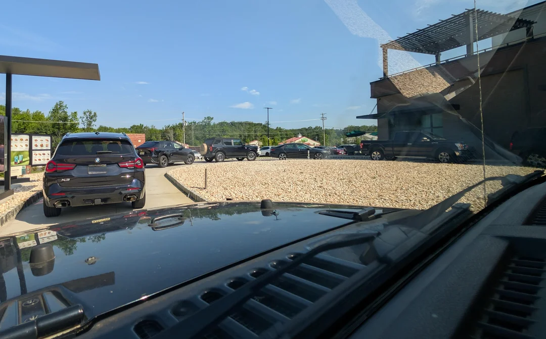 Autá stojace v rade pri drive-thru okienku počas slnečného dňa.