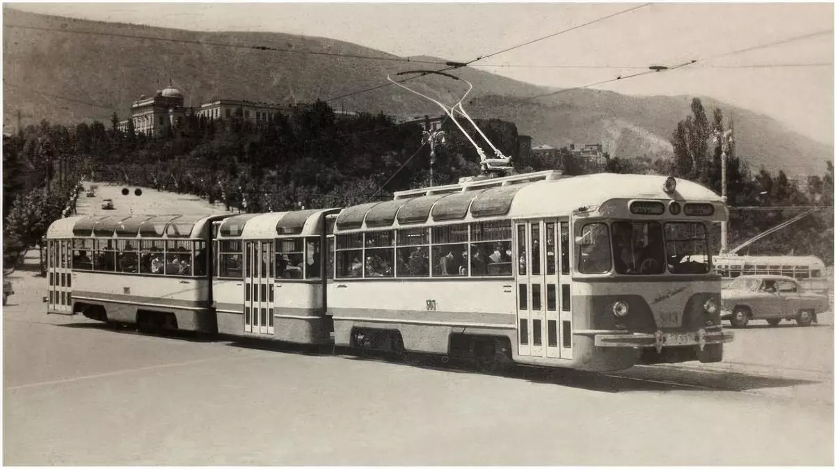 Historická električka jazdí po ulici, v pozadí sú stromy a starobylá budova, na pozadí sú kopce.