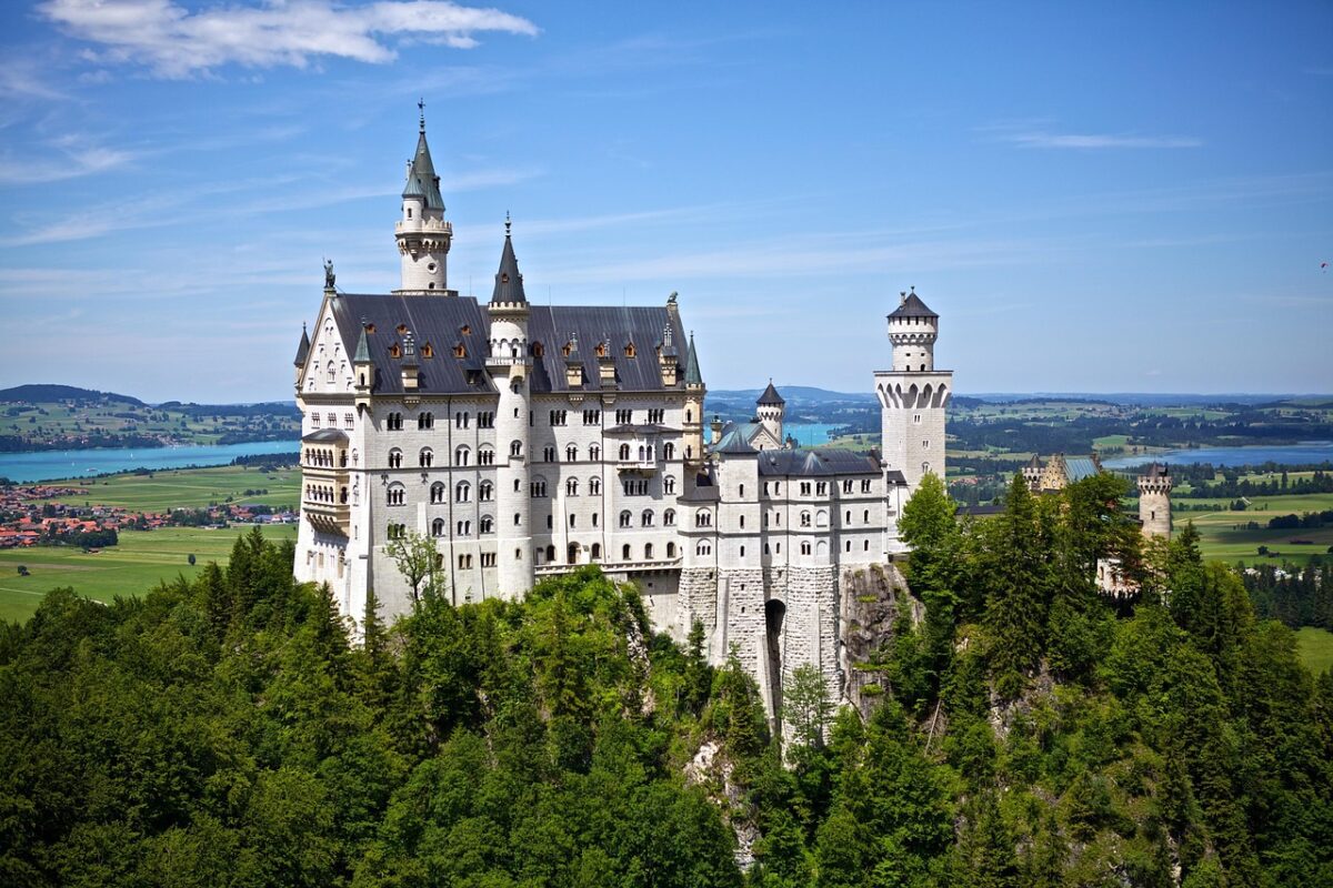 Nádherný zámok Neuschwanstein obklopený zelenými lesmi a modrou oblohou, ikonický symbol Bavorska.