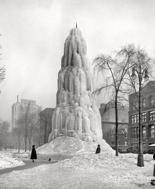 Ľadová veža v zasneženom mestskom parku, historická zimná scéna s postavami v čiernych kabátoch.