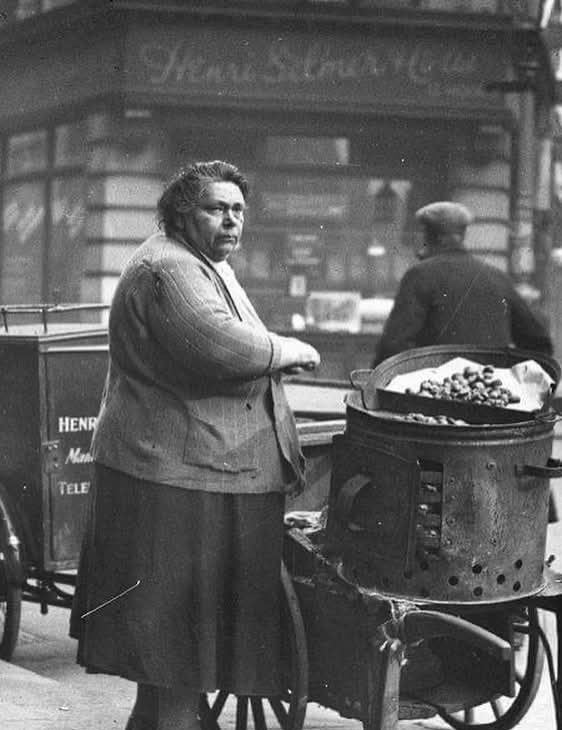 Žena predáva pečené gaštany na ulici, vintage fotografia, retro atmosféra.
