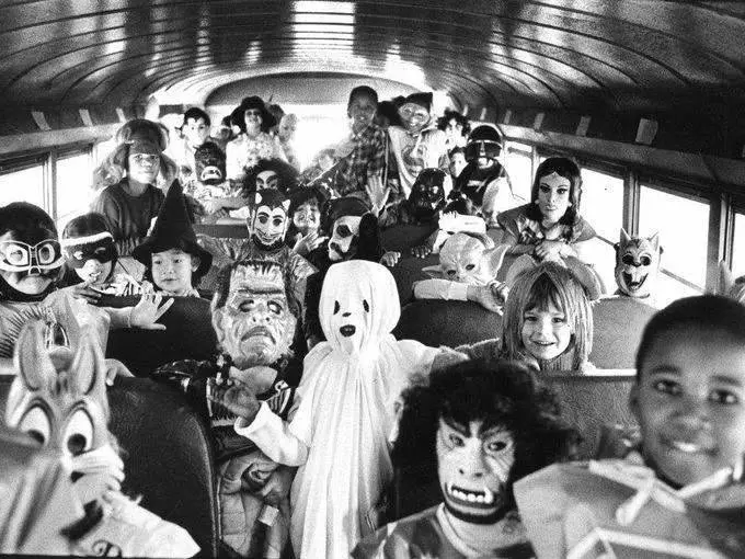 Deti v kostýmoch na Halloween v školskom autobuse, čiernobiela fotografia, plná radosti a strašidelných masiek.