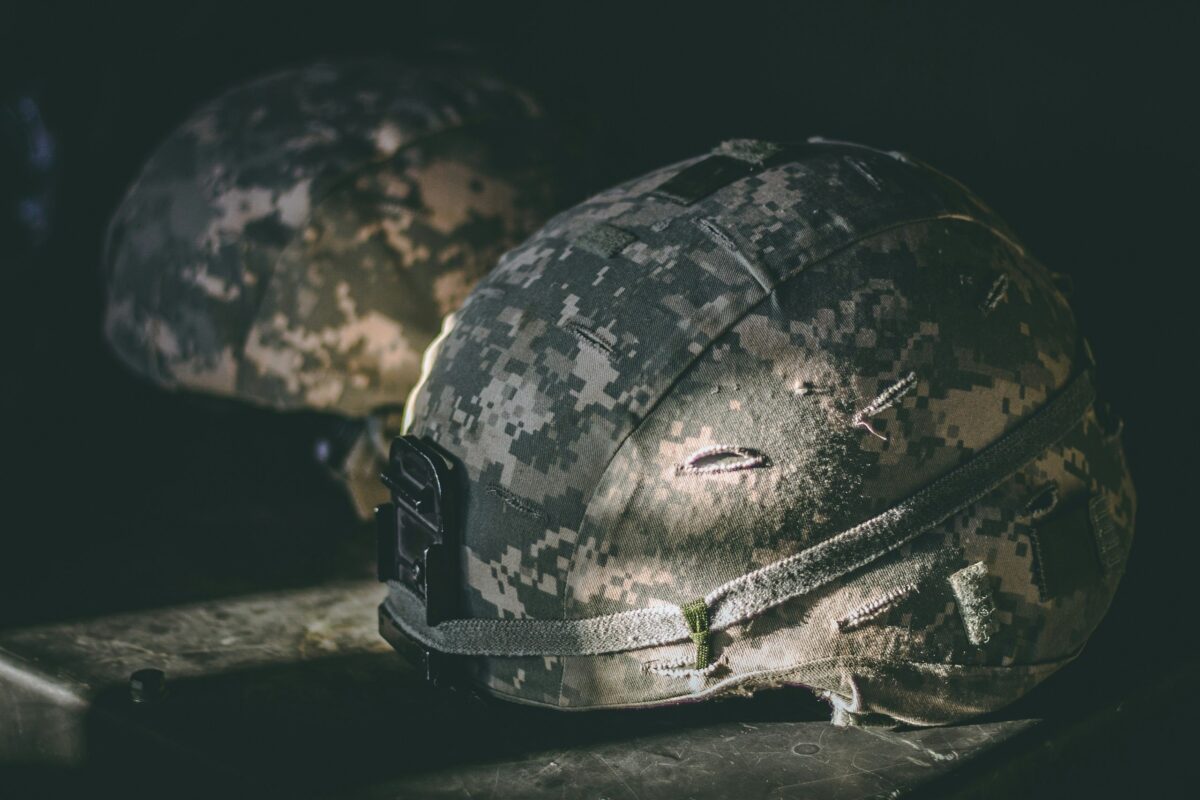 Kamuflážna vojenská prilba na tmavom pozadí, zvýraznená v dramatickom svetle.