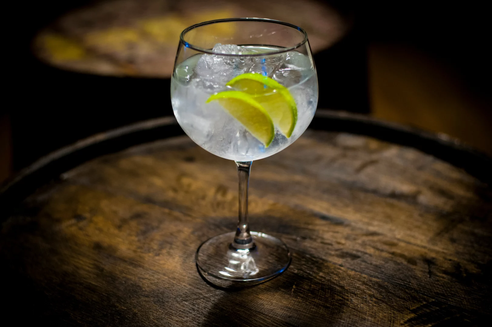 Pohár gin tonicu s plátkami limetky a ľadom na drevenom stole, podávaný na elegantnú príležitosť.