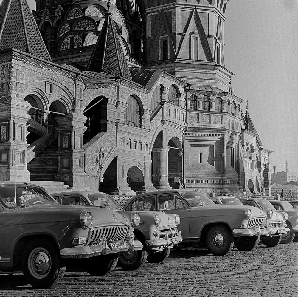 Rad historických áut zaparkovaných pred ikonickou ruskou architektúrou na dlažobných kockách.