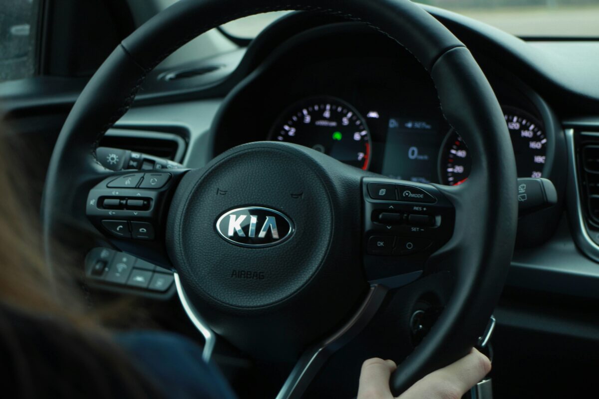 Volant automobilu Kia s viditeľnými ovládacími tlačidlami a prístrojová doska v pozadí.