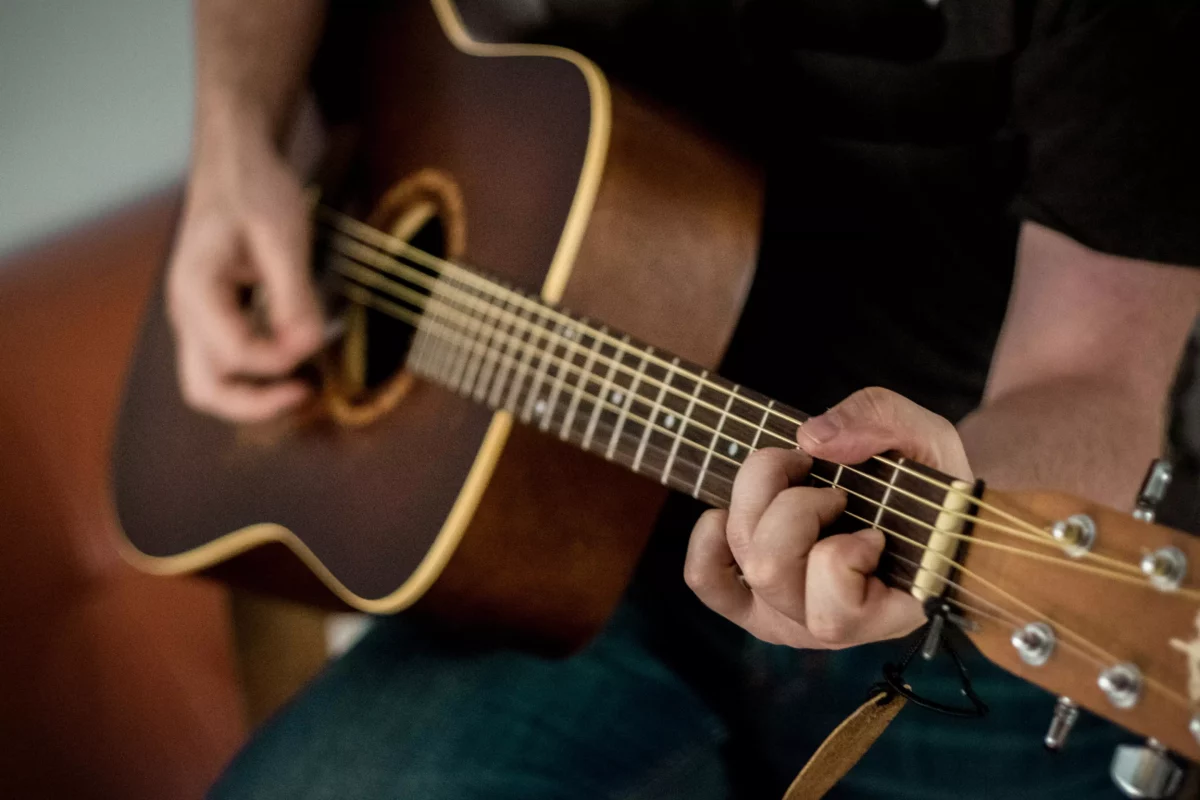 Osoba hrá na akustickej gitare, zameranie na prsty a struny, detailný pohľad na hrebeň a telo nástroja.