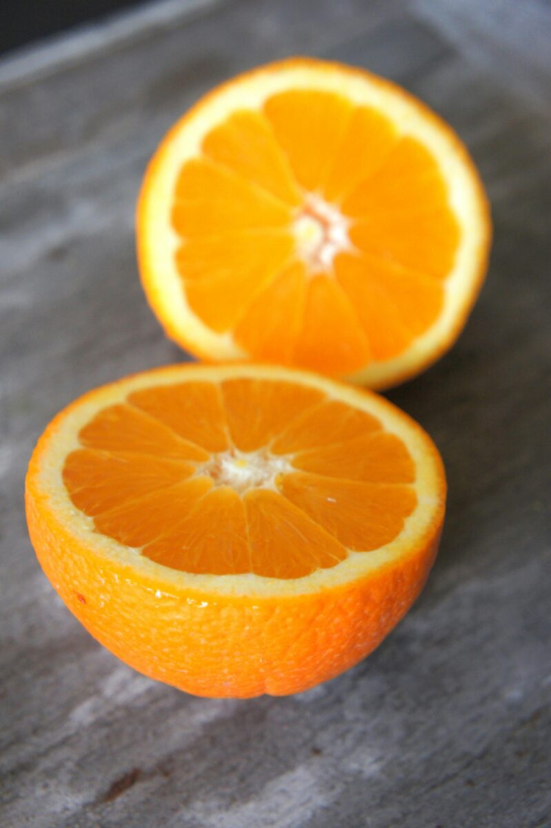 Dve polovice šťavnatého pomaranča na drevenom povrchu, detailná fotografia citrusového ovocia.